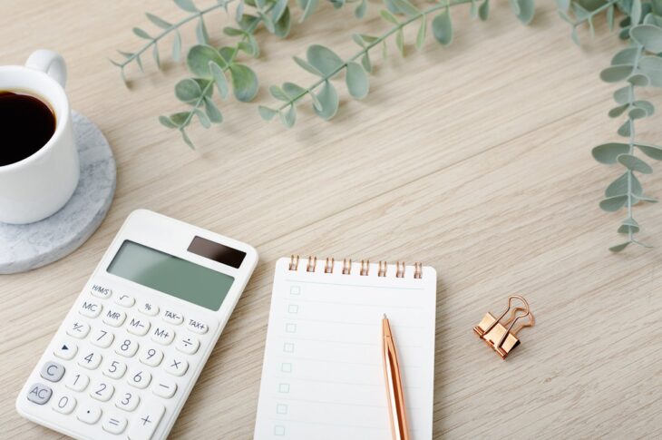 Calculator with coffee cup and notebook on light wood desk with copy space, financial planning concept