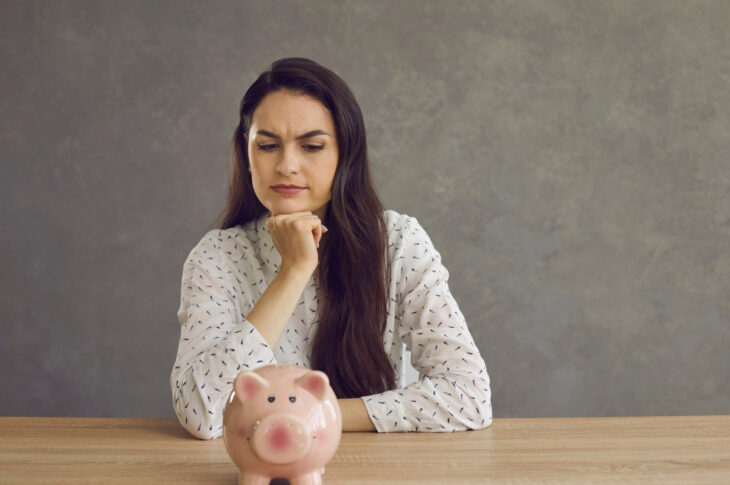 Woman sitting at a table staring at a piggy back and wondering about investing